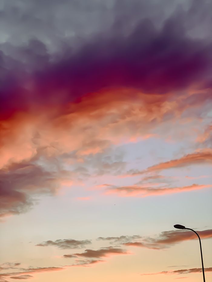 Home Dramatic purple and orange clouds at sunset over a streetlight, showcasing nature's beauty.