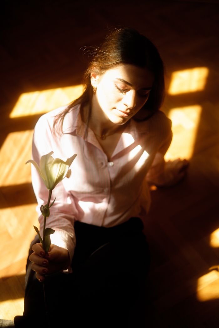 Home A serene woman holding a lily, bathed in sunlight with a warm, contemplative expression.