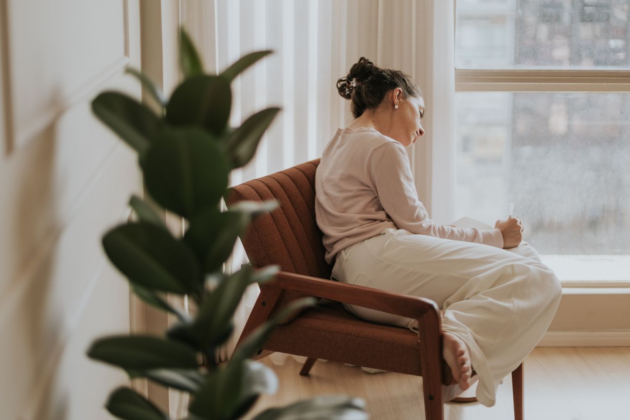 Home Woman relaxing on a chair by a window, deep in thought, indoors.