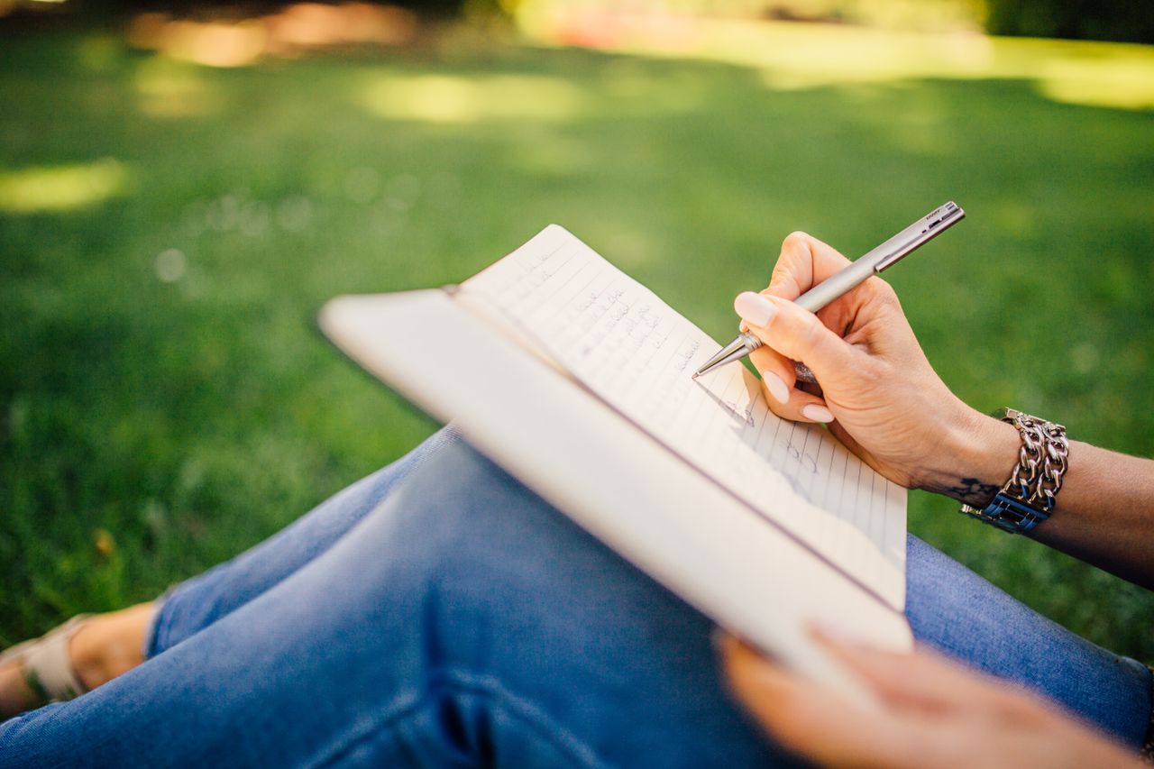 Home Person writes in a notebook on a sunny day. Focus on hands and pen outdoors.